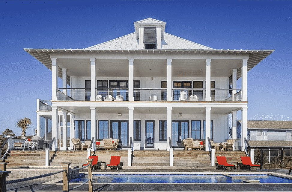 A large two story white house with a pool and dock for boats.