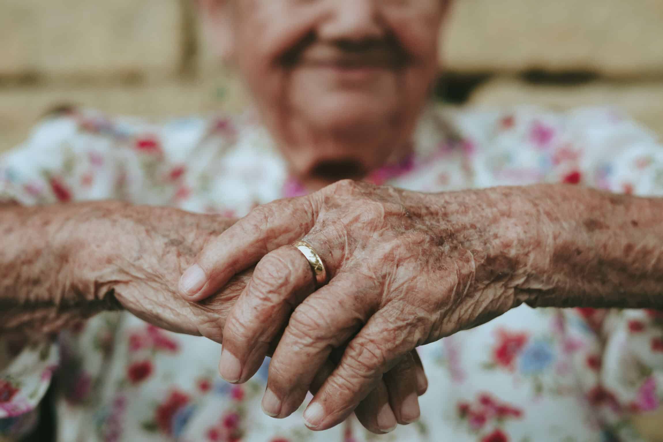 A woman’s wrinkled hands with a golden wedding ring on her middle finger.